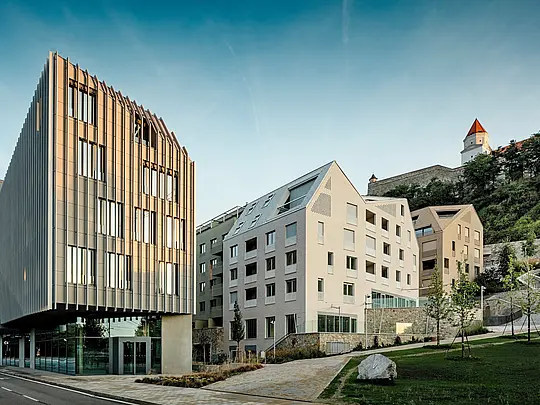 Upečatljiv spoj moderne arhitekture i povijesnog konteksta u gradskoj četvrti Vydrica u Bratislavi: u prvom planu plijeni pažnju skulpturalni volumen zgrade s vertikalnom strukturom fasade, dok u pozadini strmi krovovi s PREFA aluminijskim krovnim šindrama u bojama Prefa bijela i pješčano smeđa stvaraju precizno oblikovane naglaske. Jasno strukturirane krovne površine s integriranim prozorima tvore snažan vizualni kontrast kulisi dvorca na obronku.  PREFA aluminij odlikuje se visokom oblikovnošću, dugotrajnošću i iznimnom otpornošću na vremenske uvjete – idealno rješenje za arhitektonski zahtjevne gradske projekte.
