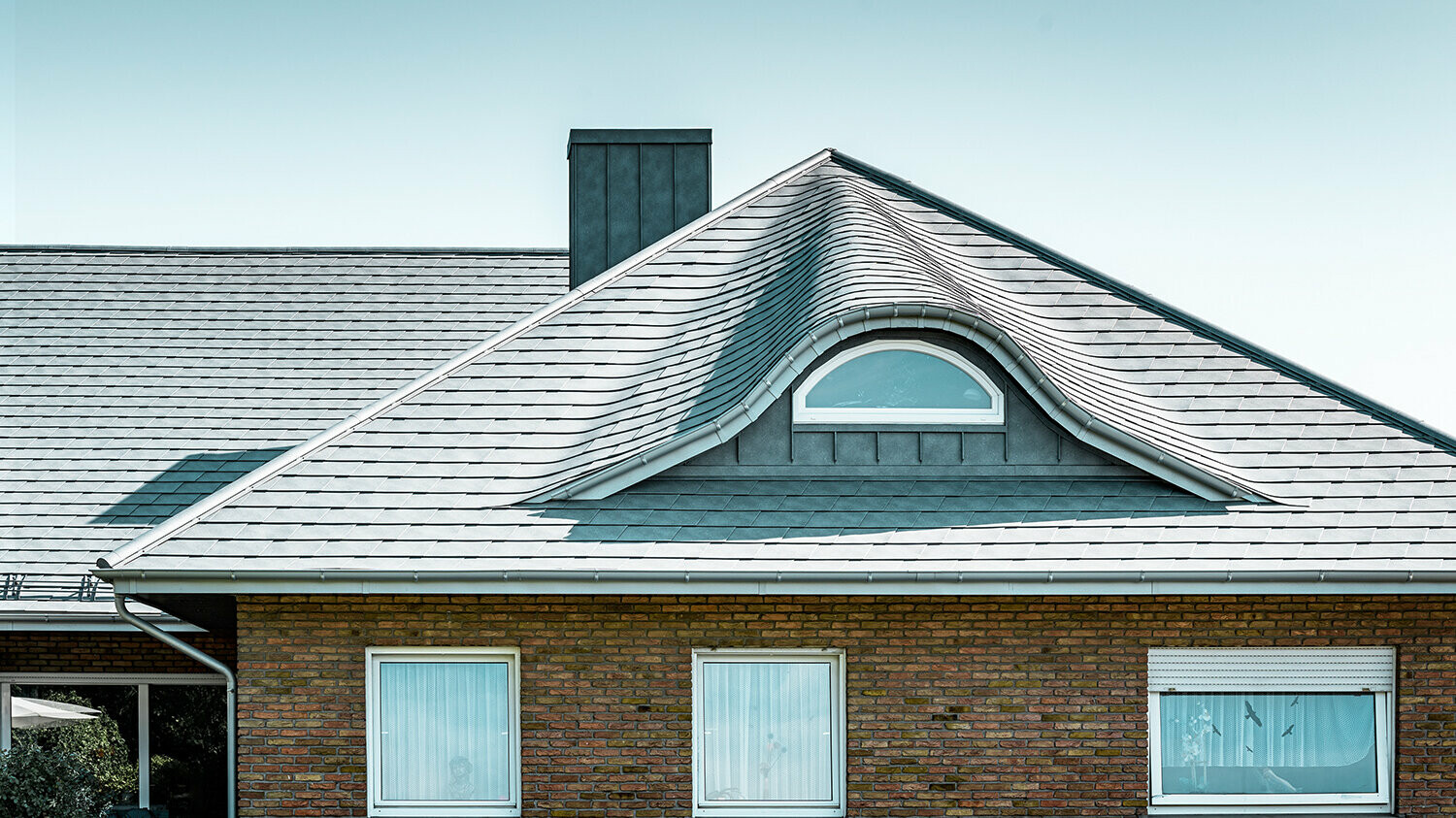 Obiteljska kuća iz 70-ih s krovom od šindre od aluminija u P.10 kameno sivoj boji sa zaobljenom krovnom kućicom s okruglim prozorom