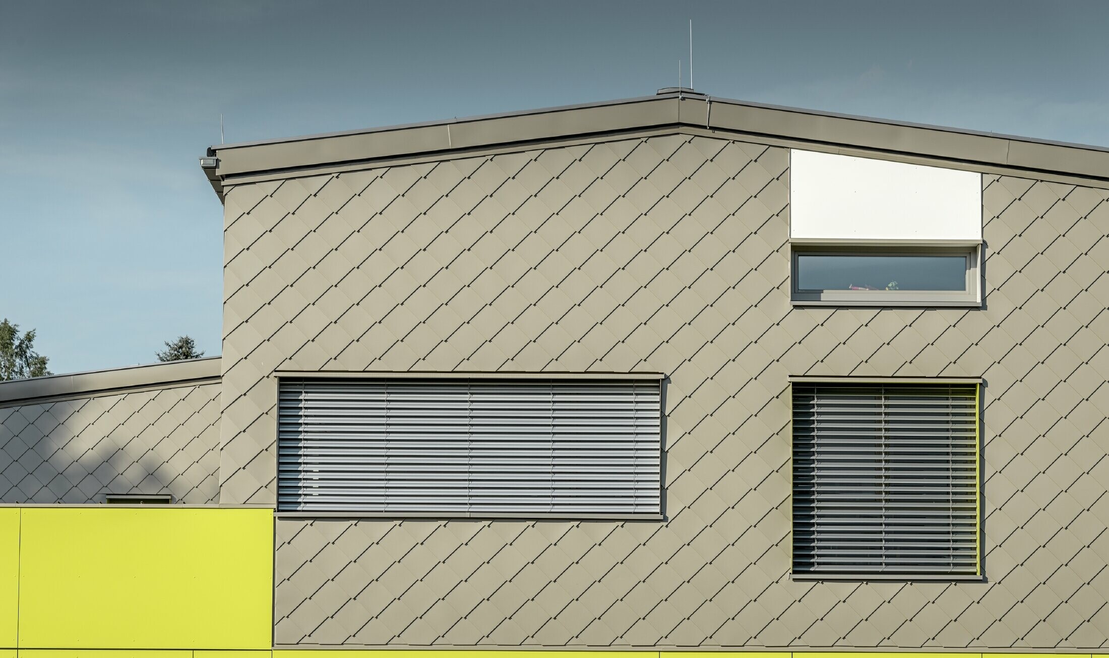 Prikaz detalja fasade s PREFA zidnim rombom 29 × 29 u boji bronce s tri prozora i bez strehe. 
