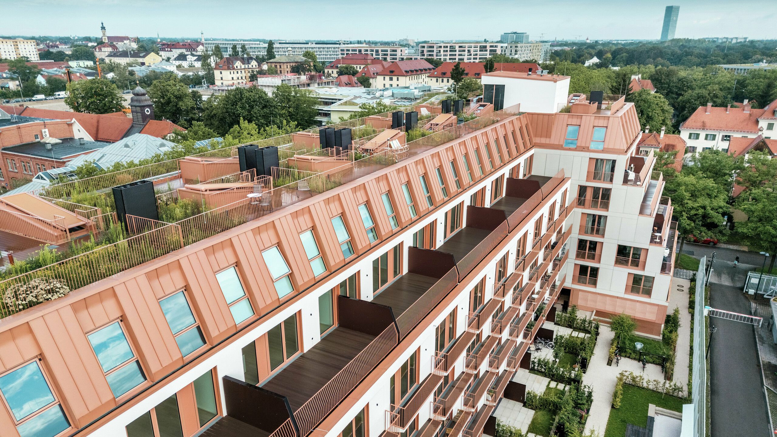 Zračni prikaz stambenog projekta Van B u Münchenu s upečatljivim PREFALZ aluminijskim krovom u posebnoj boji IGP Orange HDP tvrtke PREFA. Prostrani balkoni, zeleni krovni vrtovi i precizan dizajn fasade naglašavaju promišljeni arhitektonski koncept. Idealno za održivi urbani razvoj i urbano stanovanje s visokom kvalitetom života i estetskim zahtjevima.