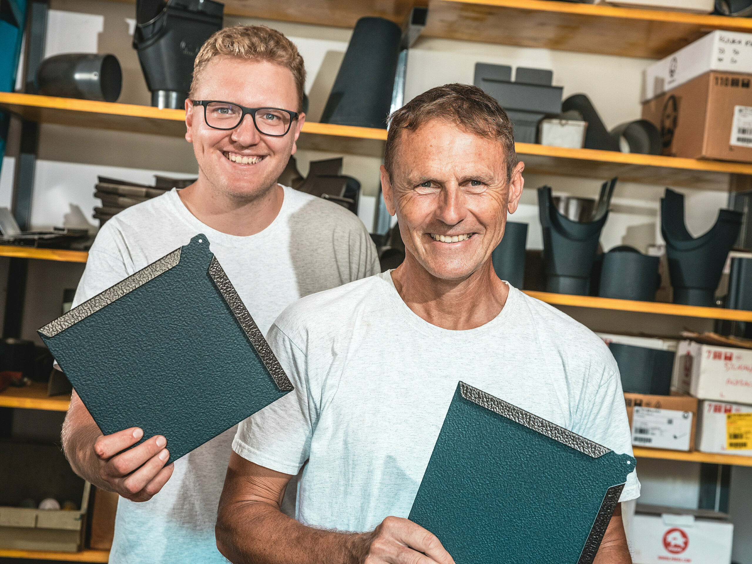 U radionici dva majstora predstavljaju kvadratne PREFA zidne rombove od aluminija u P.10 antracitnoj boji. Muškarac u prvom planu je slovenski limarski majstor Janez Kralj. Iza njega stoji mlađi član njegova tima. U pozadini se nalaze police s građevinskim elementima i priborom za krovne i fasadne sustave.  Fino strukturirana površina PREFA aluminijskih rombova svjedoči o visokoj kvaliteti materijala, dugotrajnosti i preciznoj izradi. Oni su idealni za zahtjevne arhitektonske projekte poput tiny kuća, gdje su potrebni otpornost, mala težina i moderan dizajn.