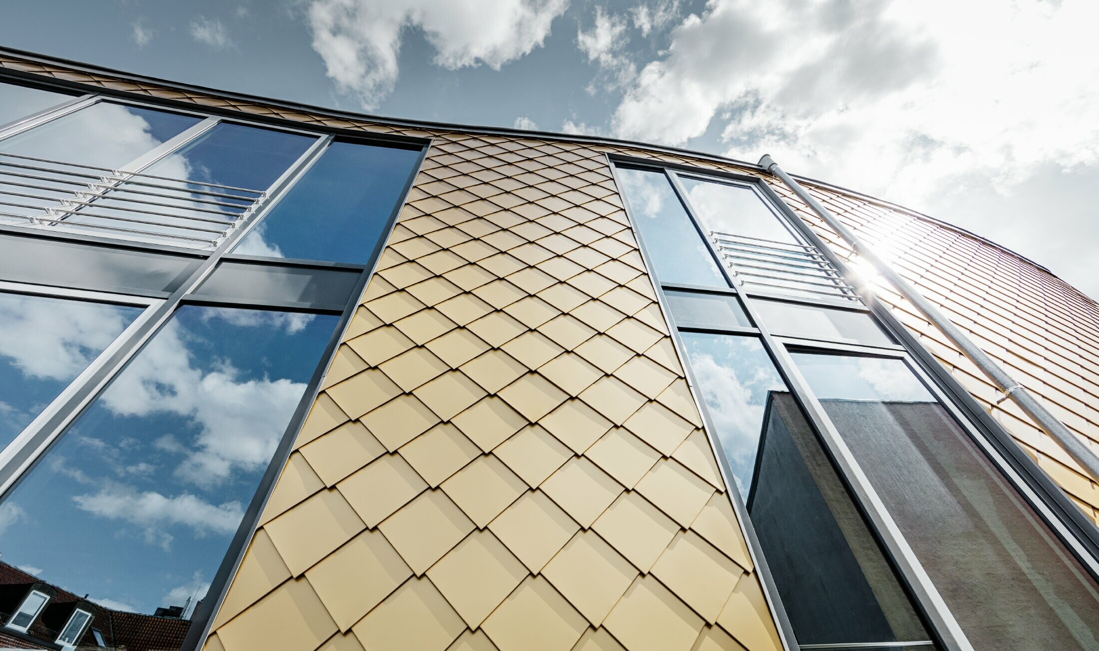 Zlatni aluminijski romb tvrtke PREFA u mayagold boji; velike staklene površine na fasadi poslovne zgrade;