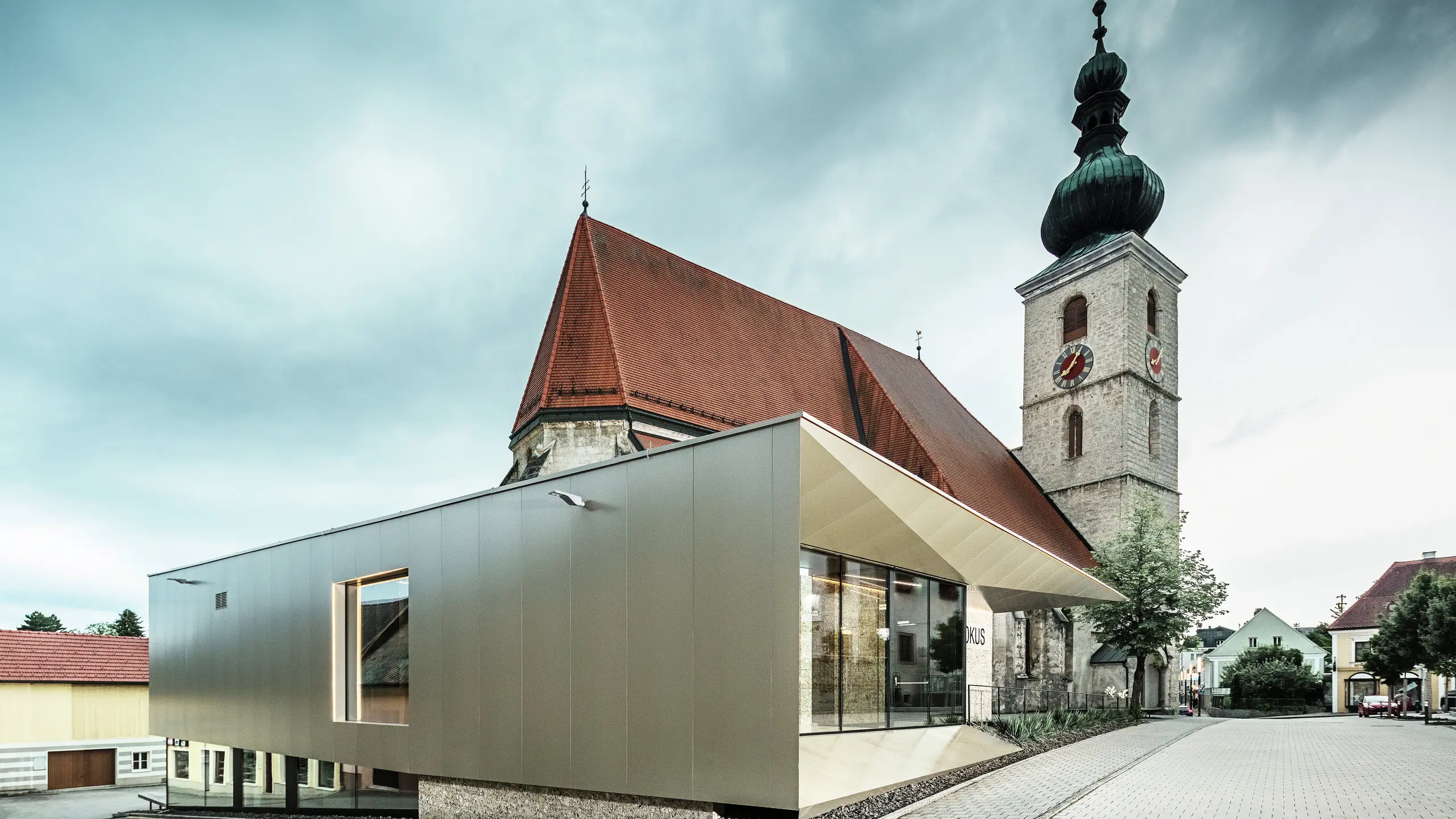 Bočni pogled prikazuje nježni krovni nadstrešnicu, izrađenu od visokokvalitetnih PREFA aluminijskih kompozitnih ploča. Precizna izrada stvara moderan izgled s čistim linijama i naglašava arhitektonsku povezanost između starog i novog.