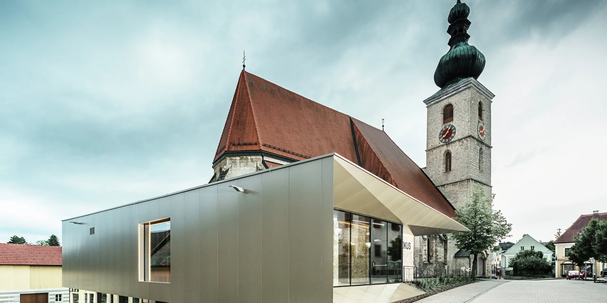 Bočni pogled prikazuje nježni krovni nadstrešnicu, izrađenu od visokokvalitetnih PREFA aluminijskih kompozitnih ploča. Precizna izrada stvara moderan izgled s čistim linijama i naglašava arhitektonsku povezanost između starog i novog.