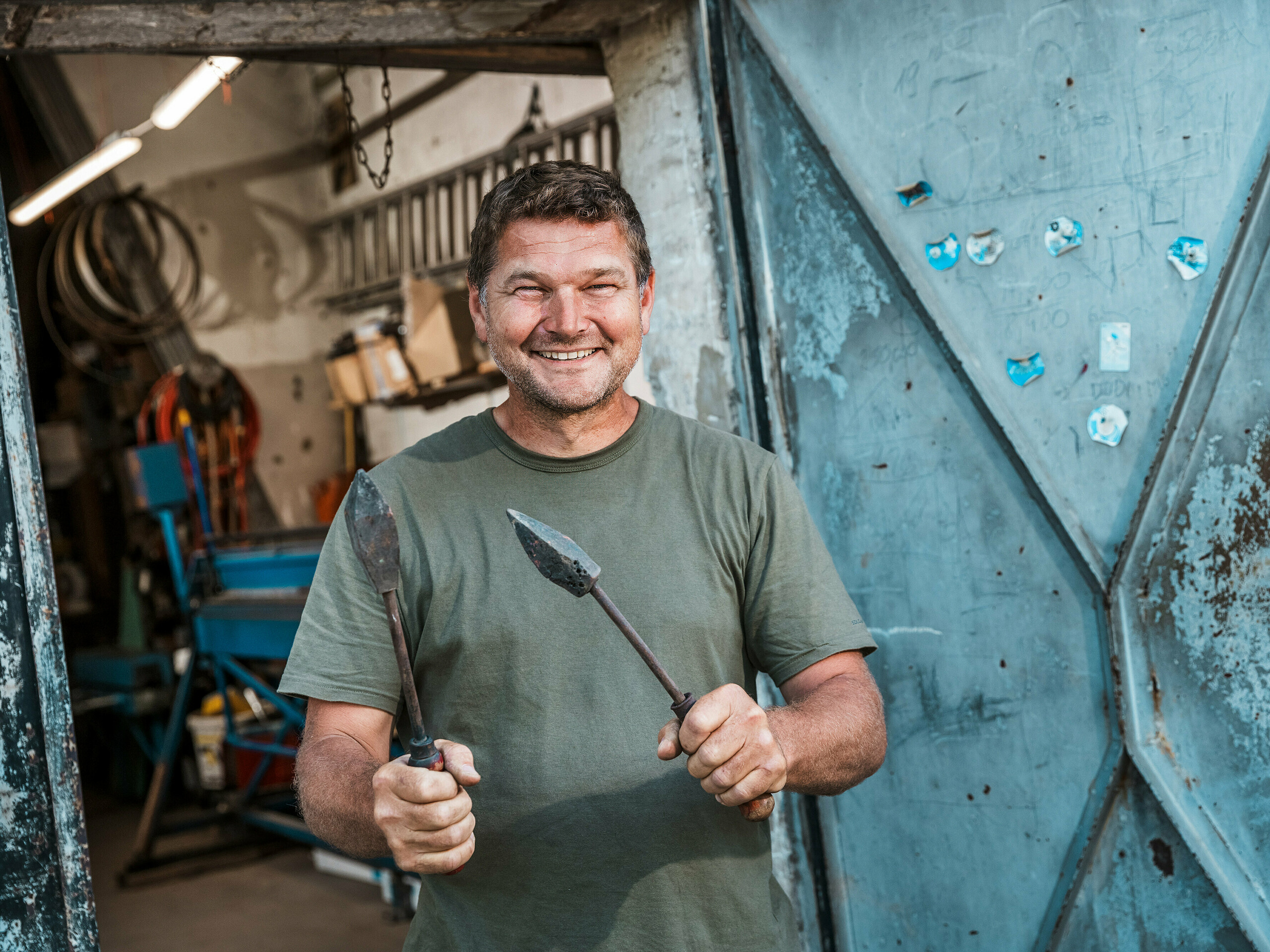 Limar Richárd Tóth u svojoj radionici. Ovaj iskusni majstor drži tradicionalni alat u rukama i stoji ispred otvorenih metalnih vrata. Scena prenosi autentičan obrtnički rad i visoku preciznost – osobine koje su bile ključne pri obradi PREFA aluminijskih proizvoda za budimpeštansku višestambenu zgradu. Sirova atmosfera radionice naglašava njegovu stručnost, kojom su izrađeni fasadni elementi, atika i obloge balkona od PREFALZ aluminija u boji P.10 antracit. Slika ističe povezanost iskustva, materijalnog znanja i dugotrajnih PREFA rješenja.
