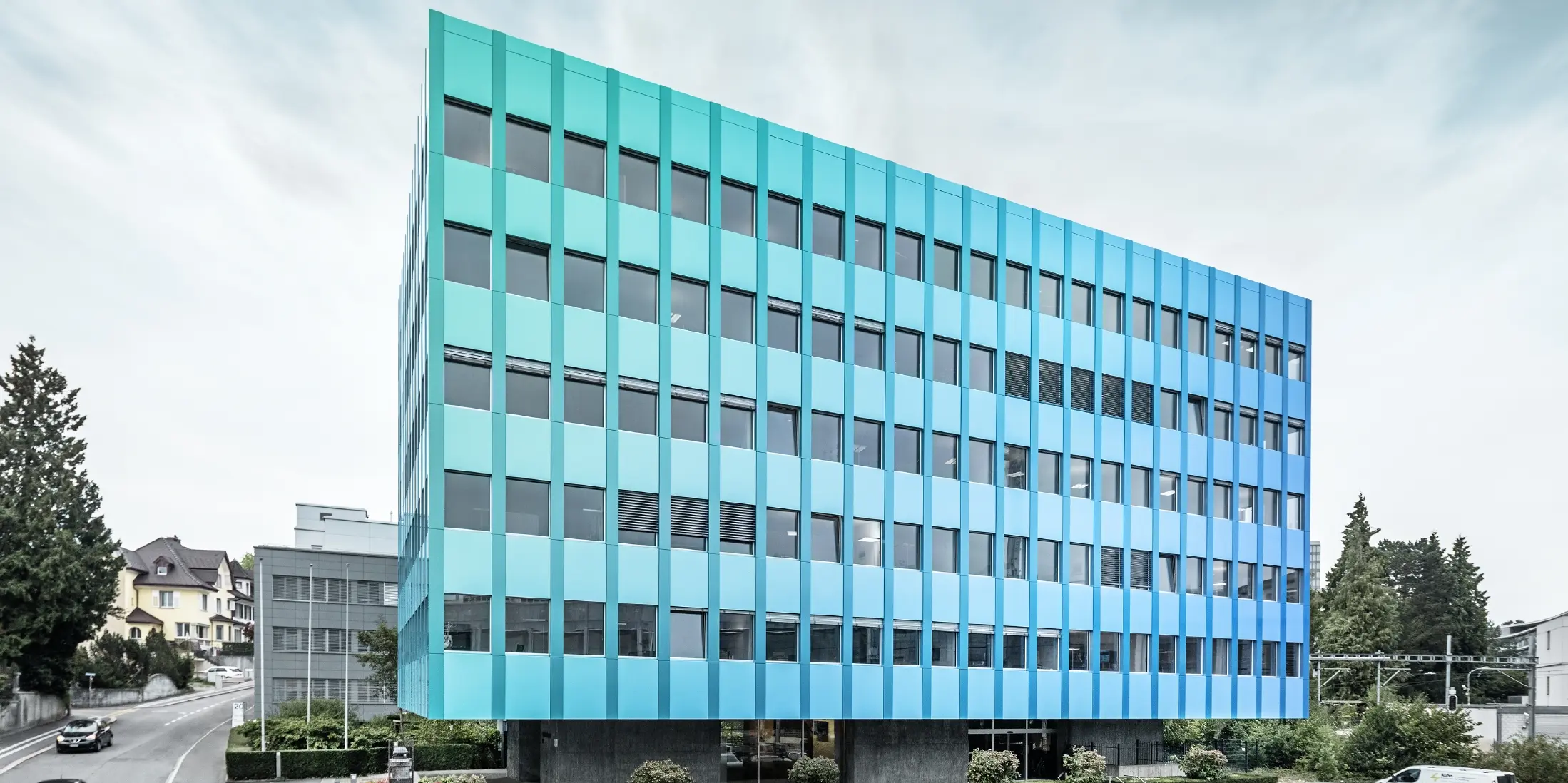 Bočni pogled na Wielandhaus u Aarauu; pročelje je obloženo kompozitnim pločama PREFABOND od aluminija tvrtke PREFA, koji blistaju u plavo-zelenoj boji zahvaljujući posebnom postupku oblaganja.
