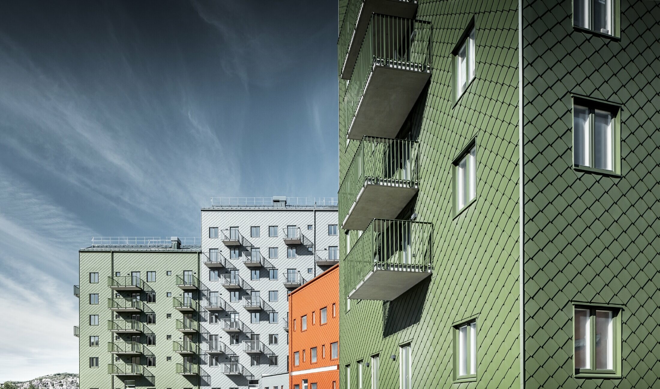 Više stambenih zgrada jedna pokraj druge, obloženih PREFA zidnim rombom 29 × 29 u bojama ciglasto crvena, maslinasto zelena i svijetlo siva.