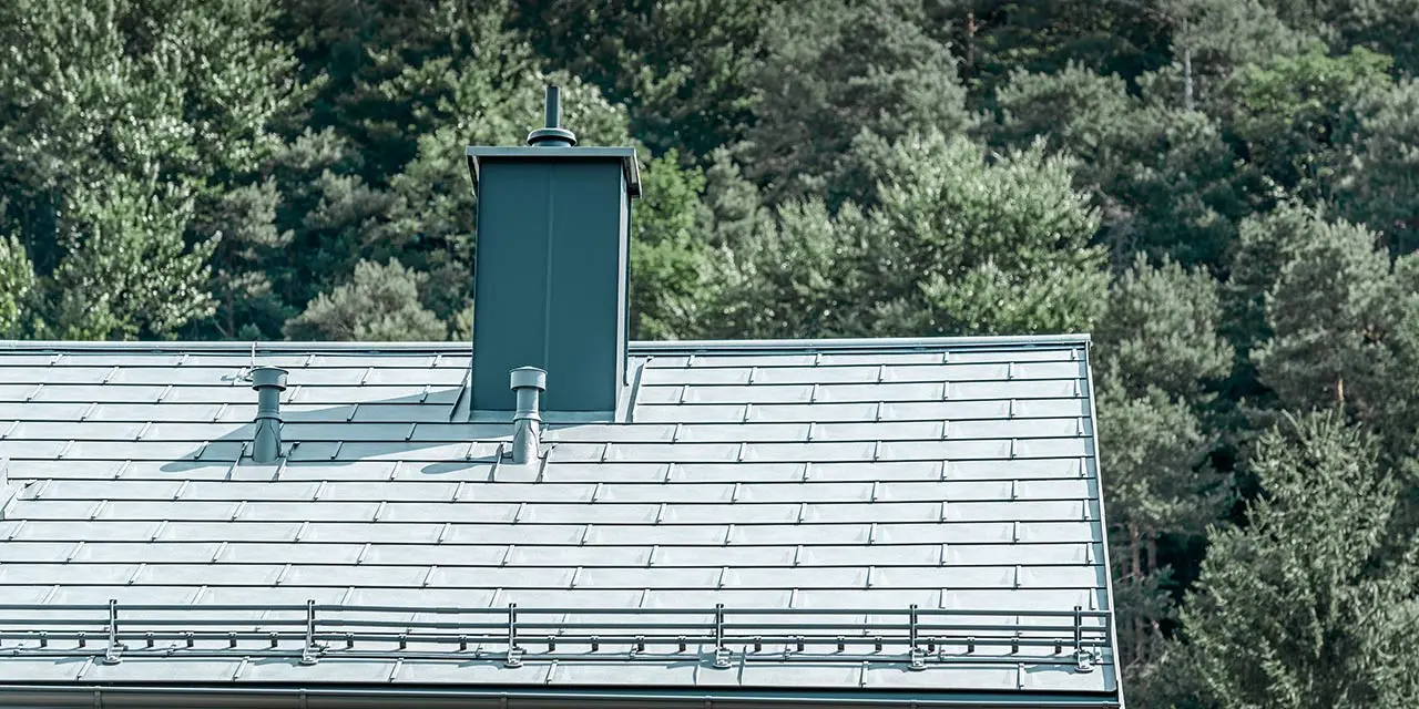 Prikaz detalja dvostrešnog krova, pokrivenog PREFA krovnom pločom R.16 u kameno sivoj sa sustavom rešetkastog snjegobrana, opšavom dimnjaka, krovnim žlijebom i odzračnom cijevi, također od tvrtke PREFA