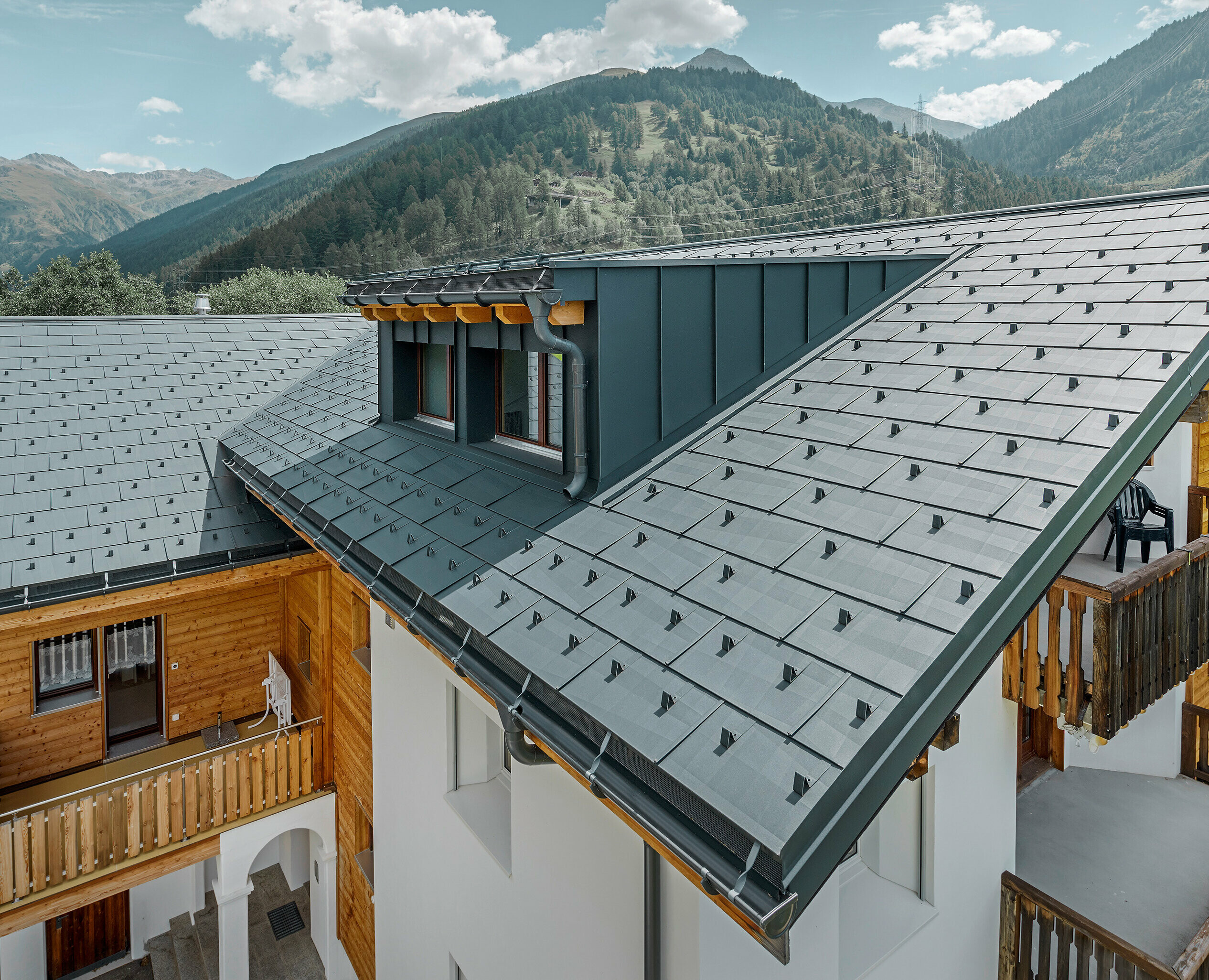Višestambena zgrada s krovnom kućicom i dvostrešnim krovom, pokrivena PREFA krovnim panelom FX.12 u antracit boji; u pozadini su vidljive planine;
