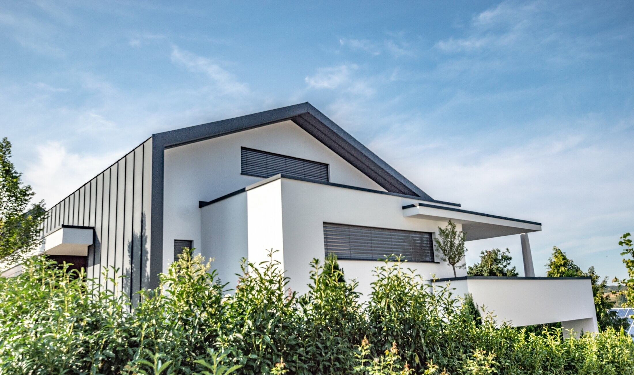 Moderna obiteljska kuća, na kojoj se krovni pokrivač kao obloga od stojećeg falca također proteže preko fasade. Boja PREFA materijala je antracit.