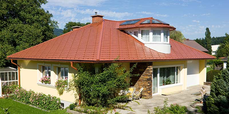 Obiteljska kuća s četverostrešnim krovom i krovnom kućicom pokrivena PREFA aluminijskom šindrom u optici crijepa, ciglasto crvenom.