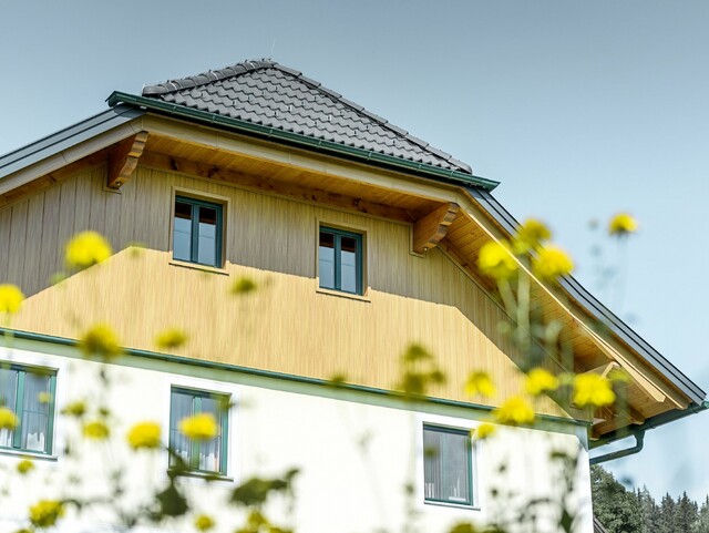 Obloga zabata s aluminijskim panelima tvrtke PREFA u optici drva (prirodni hrast), oblaganje fasadnim kazetama Siding izvedeno je vertikalno te također obuhvaća podsvođe krova