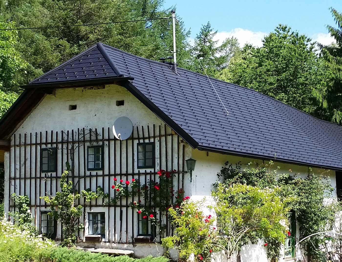 Altes traditionelles Bauernhaus mit Krüppelwalmdach; Das Dach wurde mit der Aluschindel in Schwarz von PREFA neu eingedeckt, an der Fassade ranken sich Kletterpflanzen hoch.