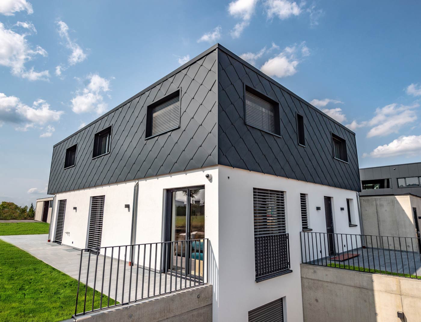 Referentni objekt PREFA zidni romb 44 × 44 antracit Moderna novogradnja s ravnim krovom - fasada gornjeg kata obložena je PREFA aluminijskim zidnim rombom 44 × 44 u antracit boji. Donji dio fasade je bijela žbuka.